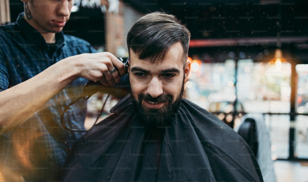 Gut aussehender junger Erwachsener, der von einem professionellen Friseur ein Haar- und Bartstyling und eine Verbandsbehandlung erhält.