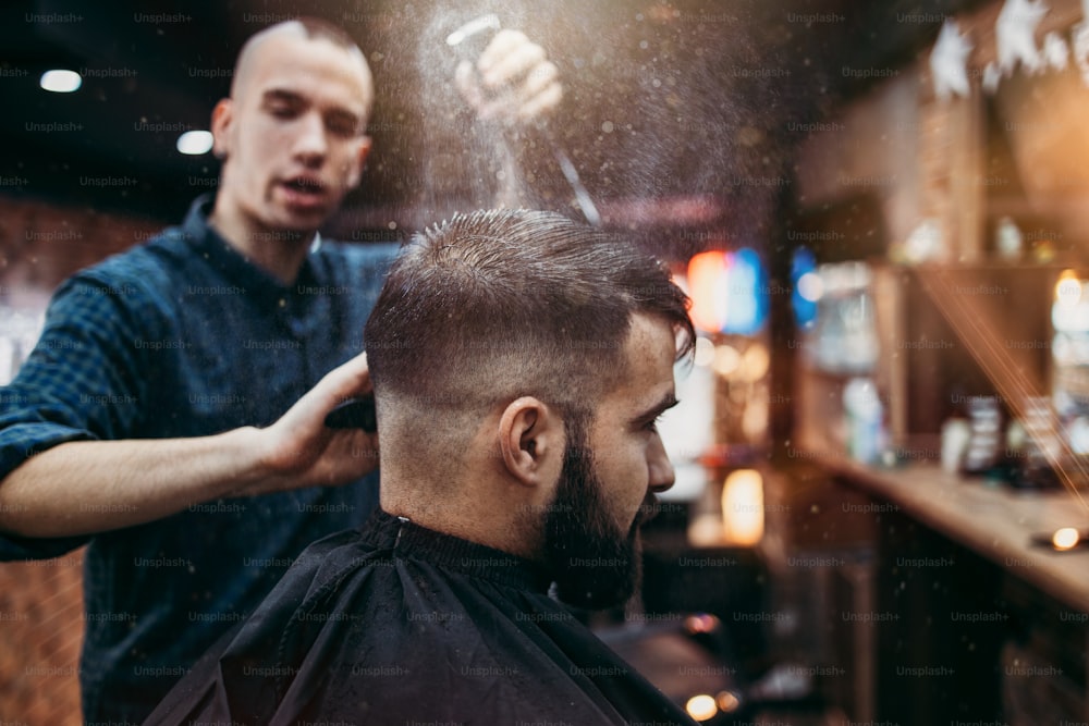 Homem jovem adulto de boa aparência recebendo um estilo de cabelo e barba e tratamento de curativo por cabeleireiro profissional.
