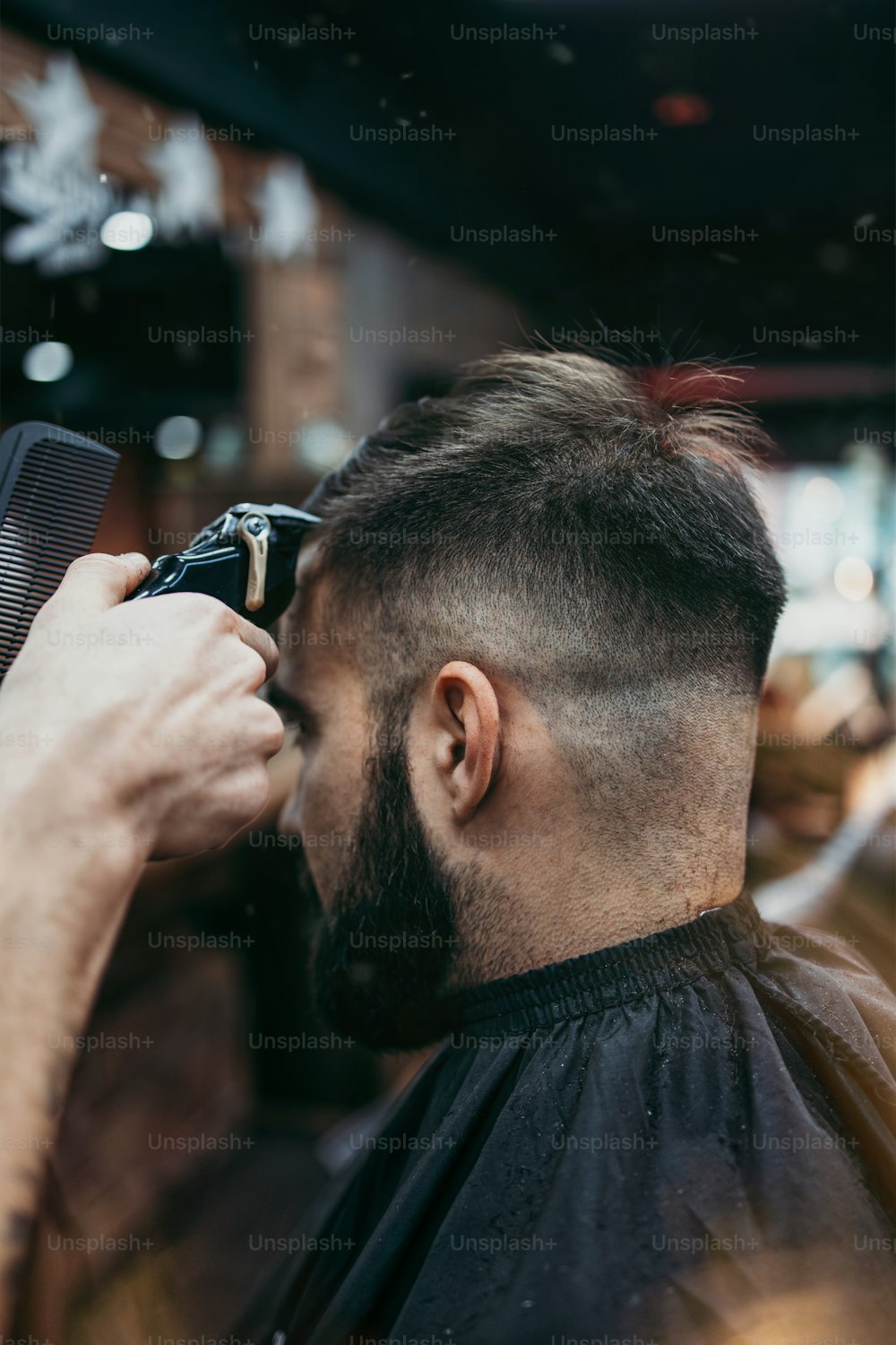 Good looking young adult man getting a hair and beard styling and dressing treatment by professional hairstylist.