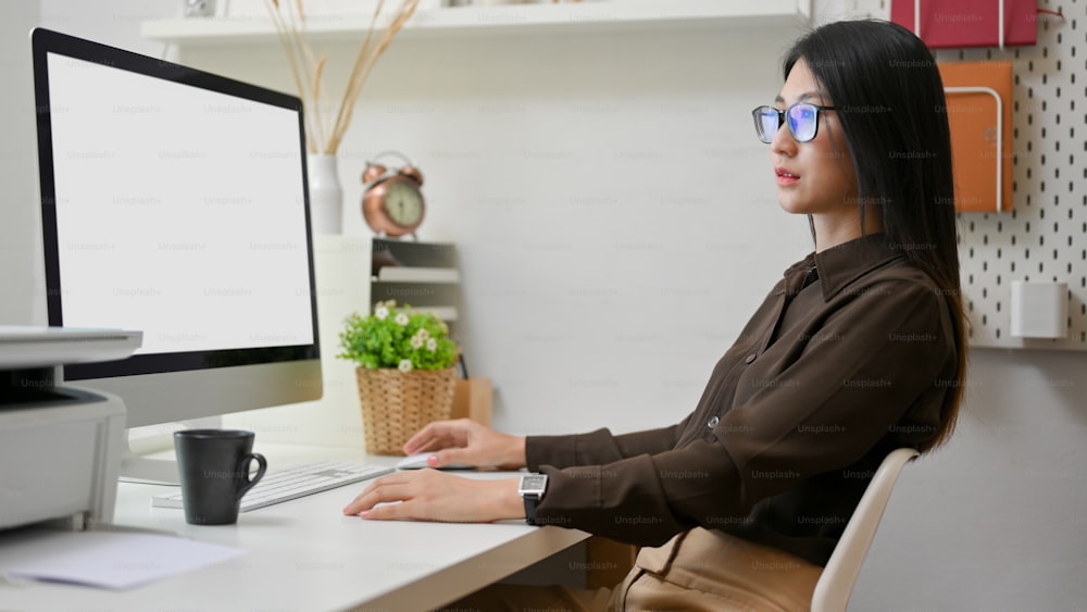 Vista lateral de una trabajadora de oficina que se concentra en su trabajo con un dispositivo informático en una sala de oficina moderna, ruta de recorte