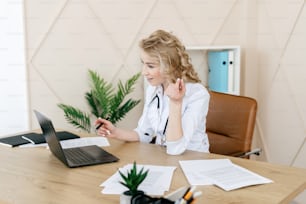 Concepto de consulta en línea. Mujer doctora que usa una computadora portátil moderna, consulte al paciente en una videollamada. Enfermera con uniforme médico blanco que trabaja en una clínica privada, sentada detrás del escritorio en la oficina
