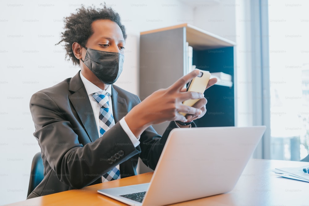 사무실에서 일하는 동안 얼굴 마스크를 착용하고 휴대 전화를 사용하는 전문 사업가. 사업 개념입니다.