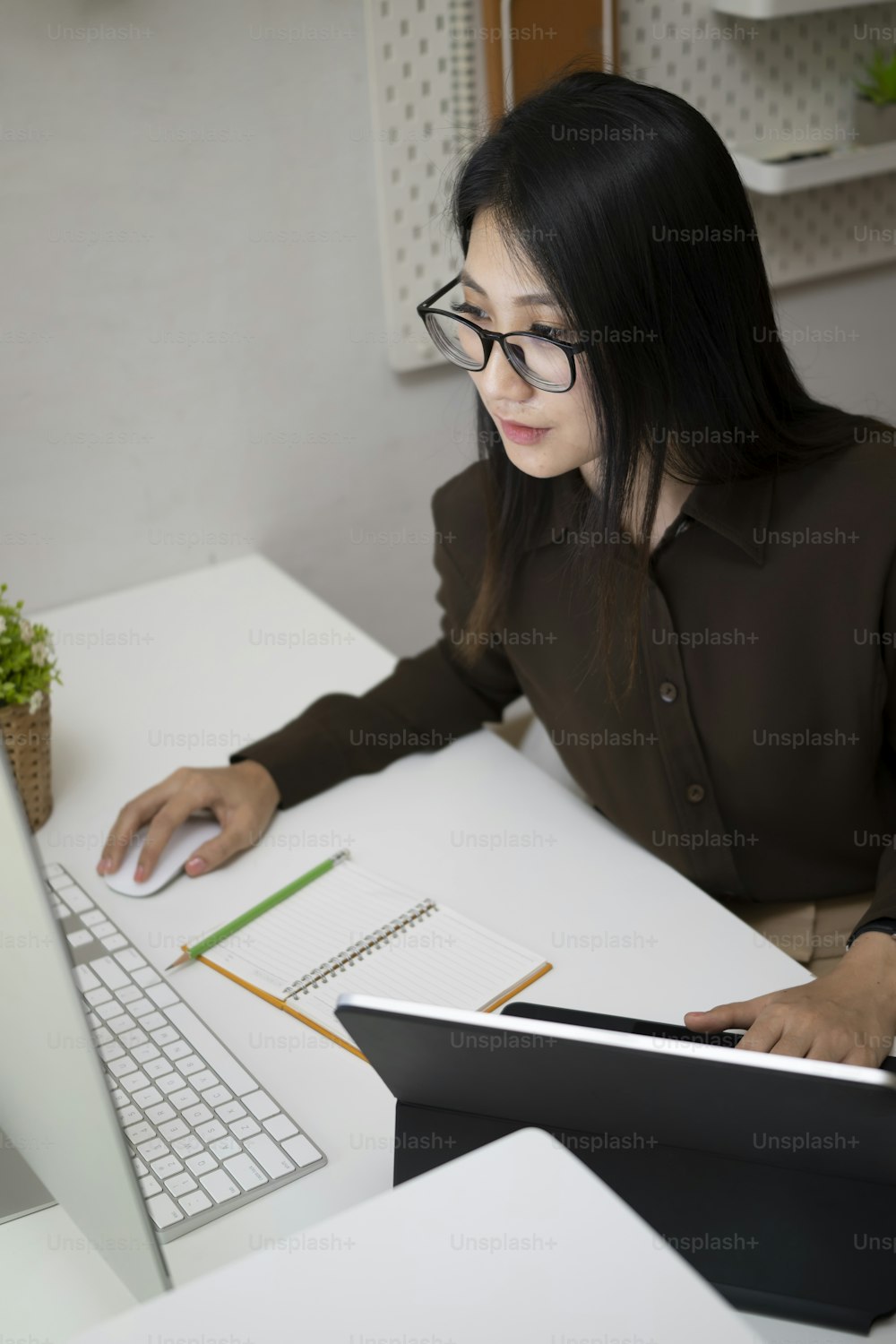 Vielbeschäftigte Geschäftsfrau, die mit mehreren Geräten im modernen Büro arbeitet.