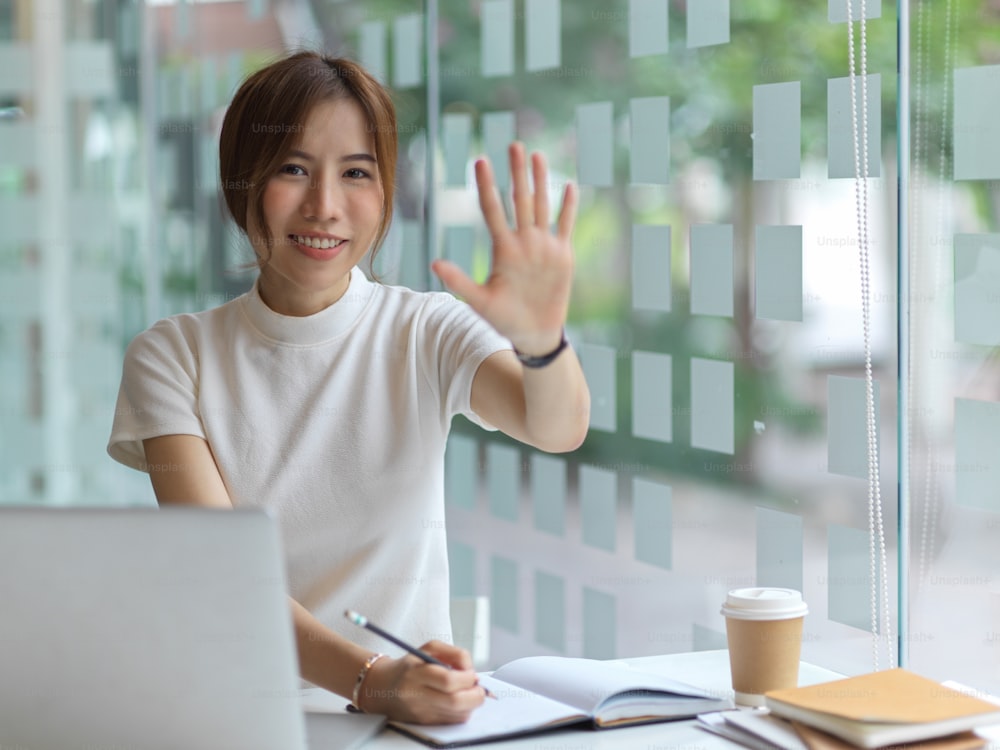 Retrato de una mujer joven bonita sonriendo y calzando cinco palmas que dejan la mano a la cámara mientras trabajan en un lugar de trabajo moderno