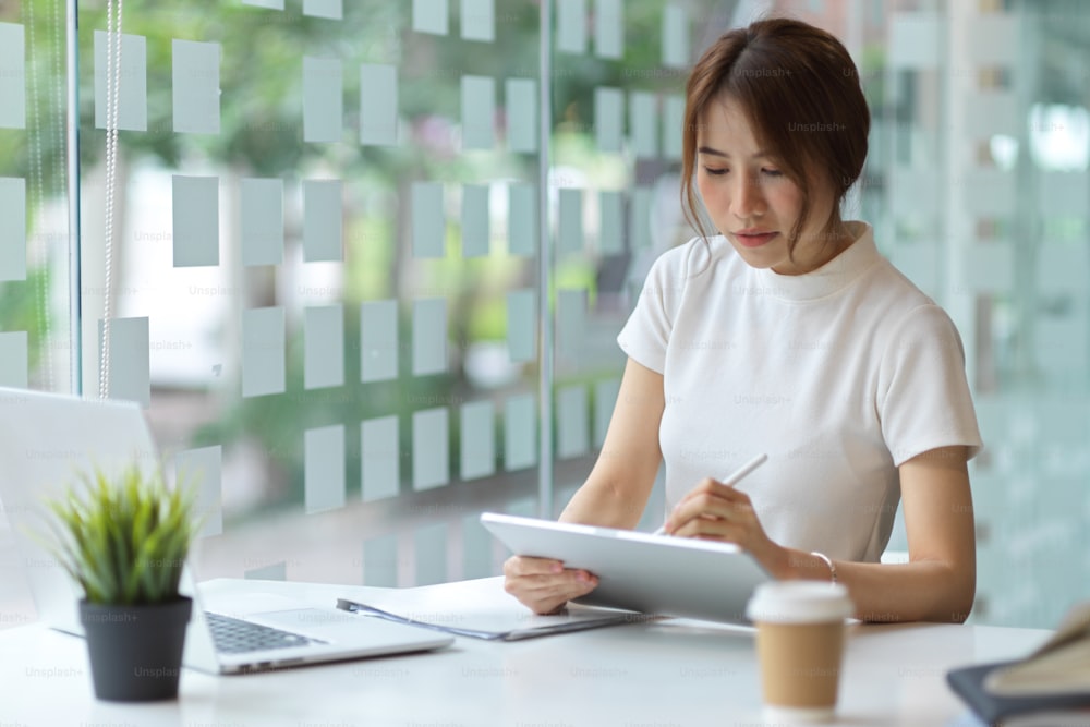 Portrait of young pretty female using digital tablet while working in modern workplace