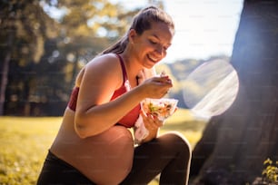 Pregnant woman eating salad after exercise in the park.