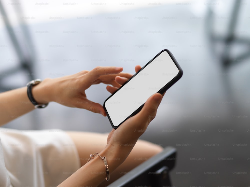 Cropped shot of a woman using smartphone include clipping path screen in her hands while sitting on the armchair