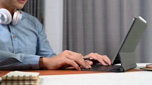 Cropped shot of young man freelancer with headphone working online on computer tablet.
