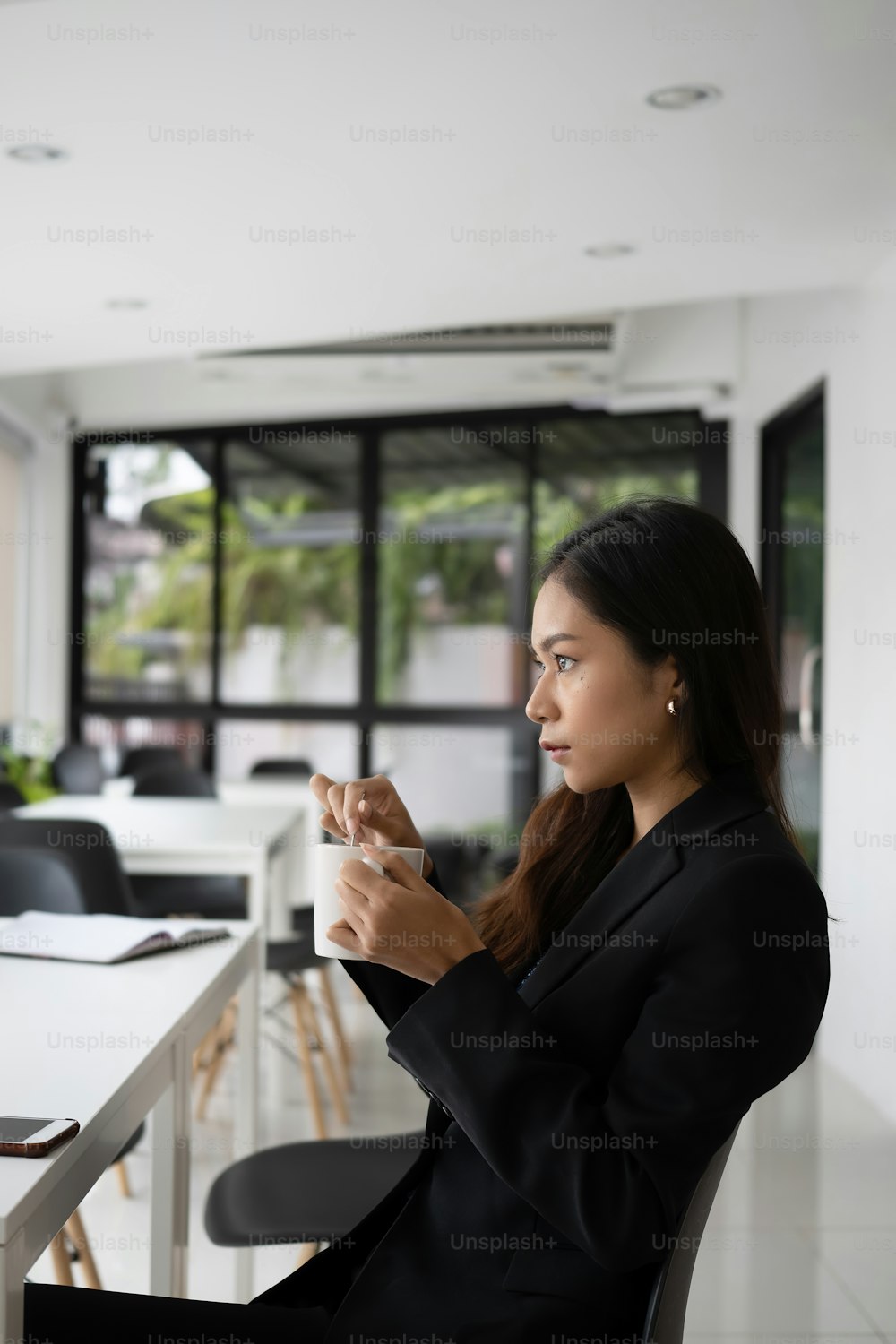 Ritratto di donna d'affari premurosa che tiene la tazza di caffè guardando avanti attraverso la finestra di vetro sul suo posto di lavoro.