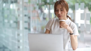 Ritratto a mezzo busto di giovane bella femmina che tiene una tazza di caffè e lavora con il laptop in uno spazio di co-working