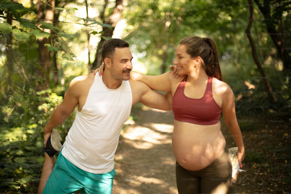 The coach helps a pregnant woman during exercises in the park.