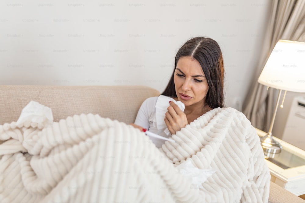Sickness, seasonal virus problem concept. Woman being sick having flu lying on sofa looking at temperature on thermometer. Sick woman lying in bed with high fever. Corona Virus