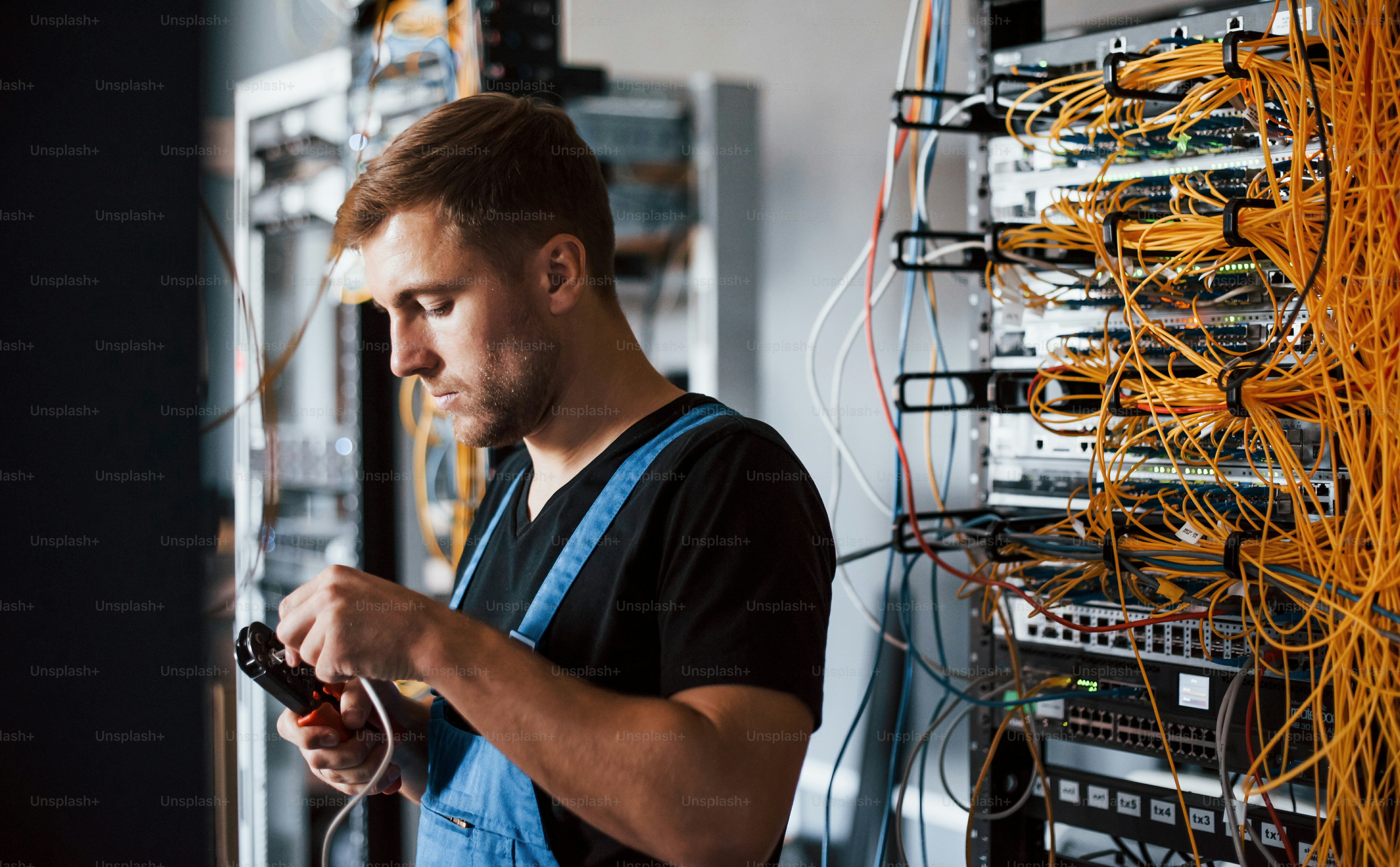 Jovem de uniforme com aparelho de medição trabalha com equipamentos de internet e fios na sala do servidor