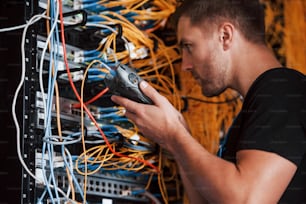 Young man in uniform works with internet equipment and wires in server room.