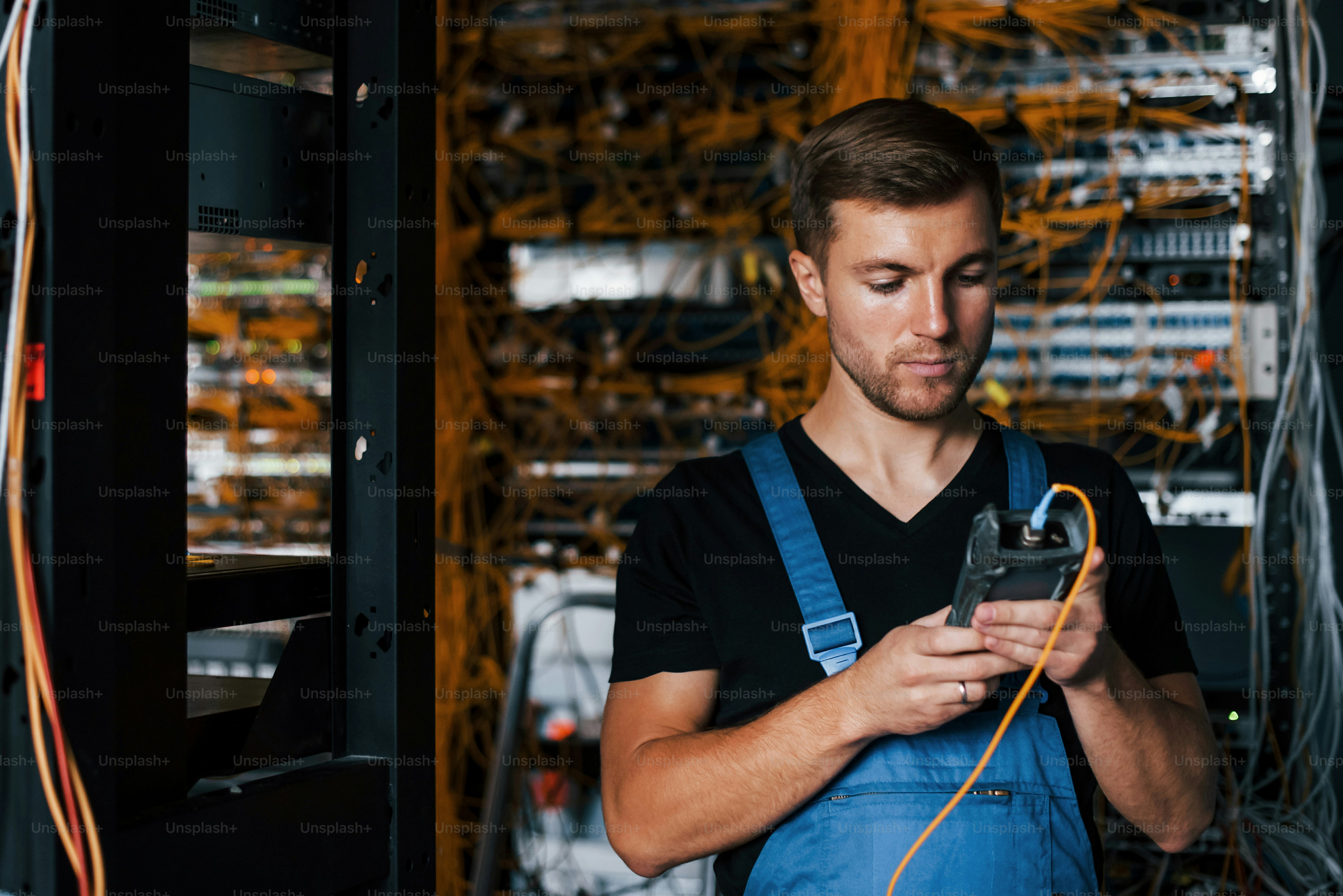Junger Mann in Uniform mit Messgerät arbeitet mit Internetgeräten und Kabeln im Serverraum.