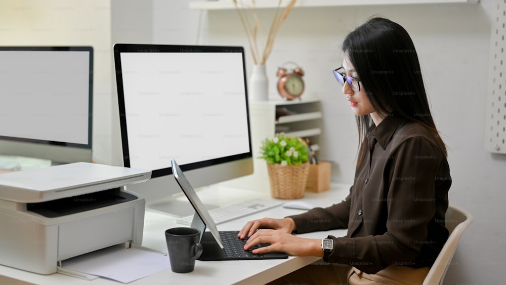 Seitenansicht einer Büroangestellten, die mit einem digitalen Tablet auf dem Computertisch im Büroraum arbeitet