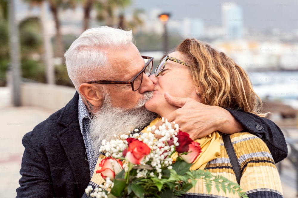 Retrato de una encantadora pareja atractiva y alegre de personas mayores abrazándose y besándose durante la fecha de aniversario. Un hombre guapo sorprendió a su esposa con flores en el día de San Valentín. Emociones de personas reales.