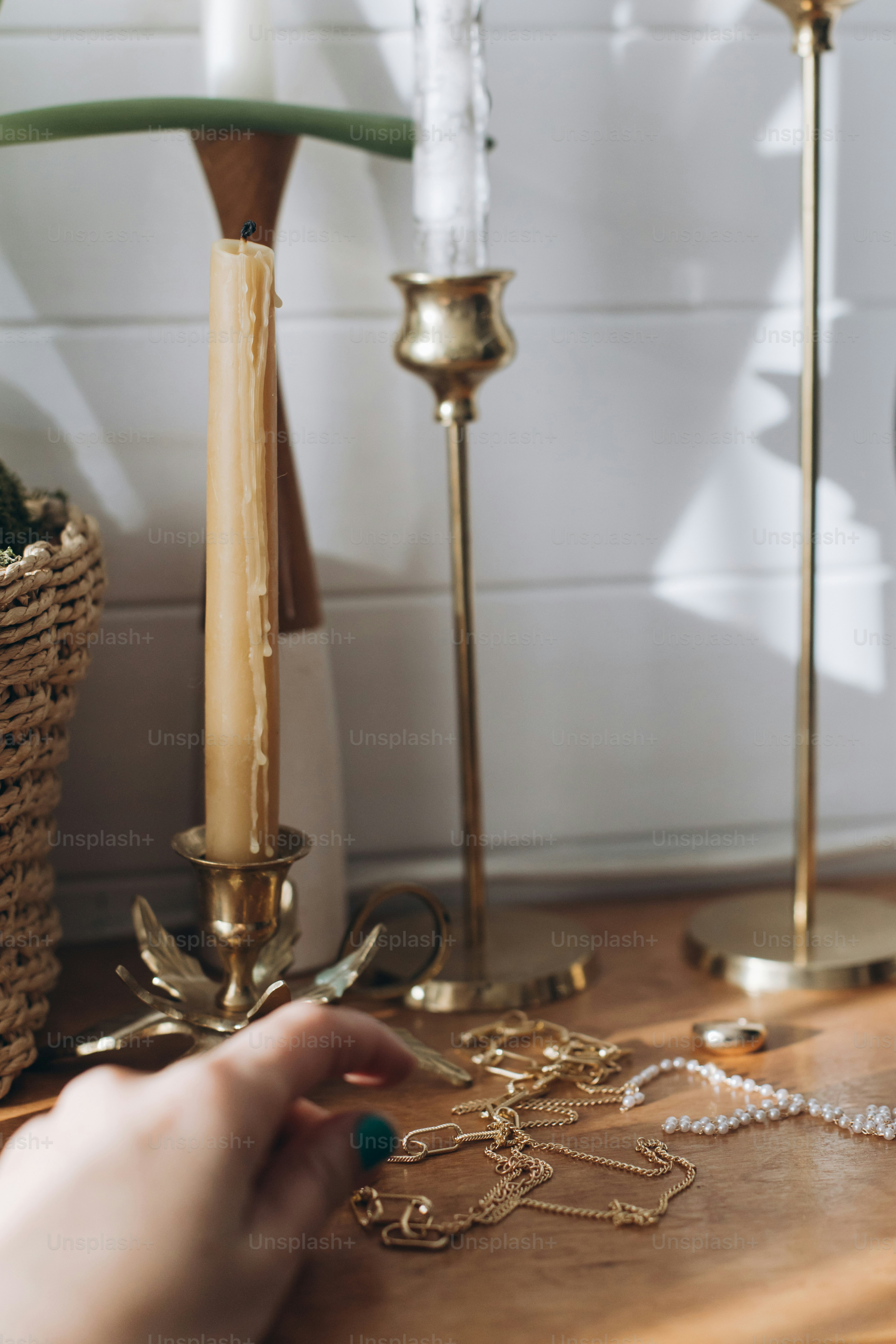 Modern gold and pearl accessories and blurred female hand on table with vintage candlesticks. Stylish golden necklace and ring on wooden background in sunny light.