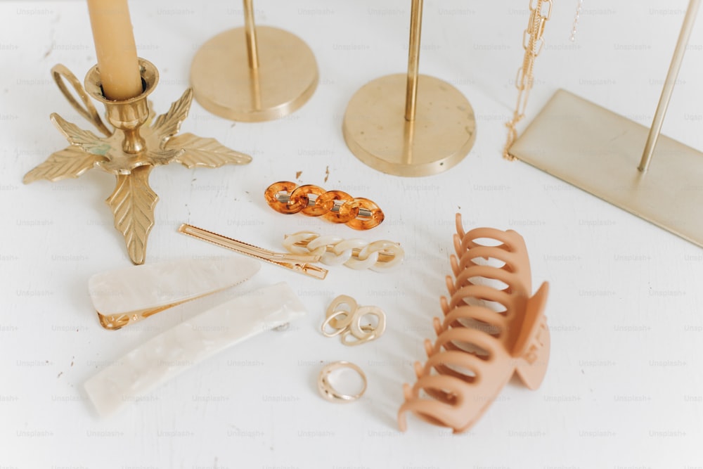 Modern golden accessories and hair clips on white table with vintage candles and boho mirror. Stylish gold ring, chain necklace, earrings, hairpins and barrettes. Boho jewellery
