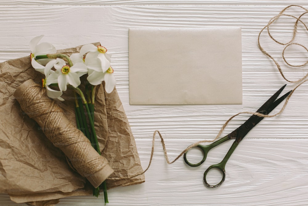 美しい水仙、グリーティングカード、はさみ、白い素朴な木製の背景に麻ひも、テキスト用のスペースとフラットレイ。母の日おめでとう。女性の日おめでとう。 花のグリーティングカードテンプレート