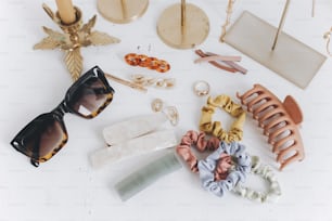 Modern golden jewellery, hair clips and hairbands, sunglasses on white table with vintage candles. Stylish gold ring, necklace, earrings, hair pins, barrettes. Summer boho accessories