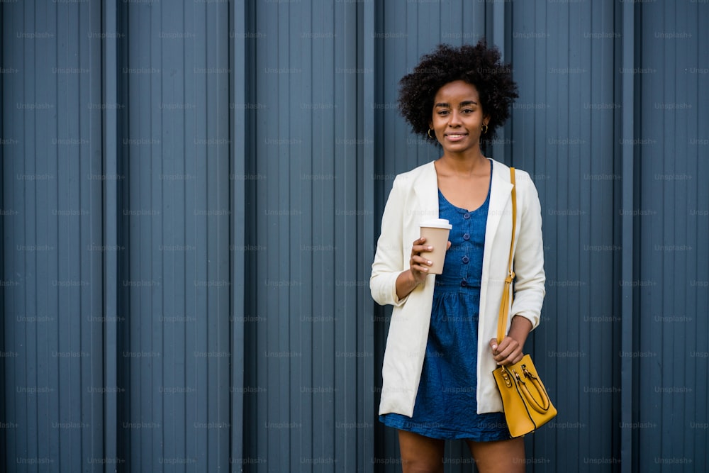 Portrait of afro business woman holding a cup of coffee while standing outdoors on the street. Business and urban concept.