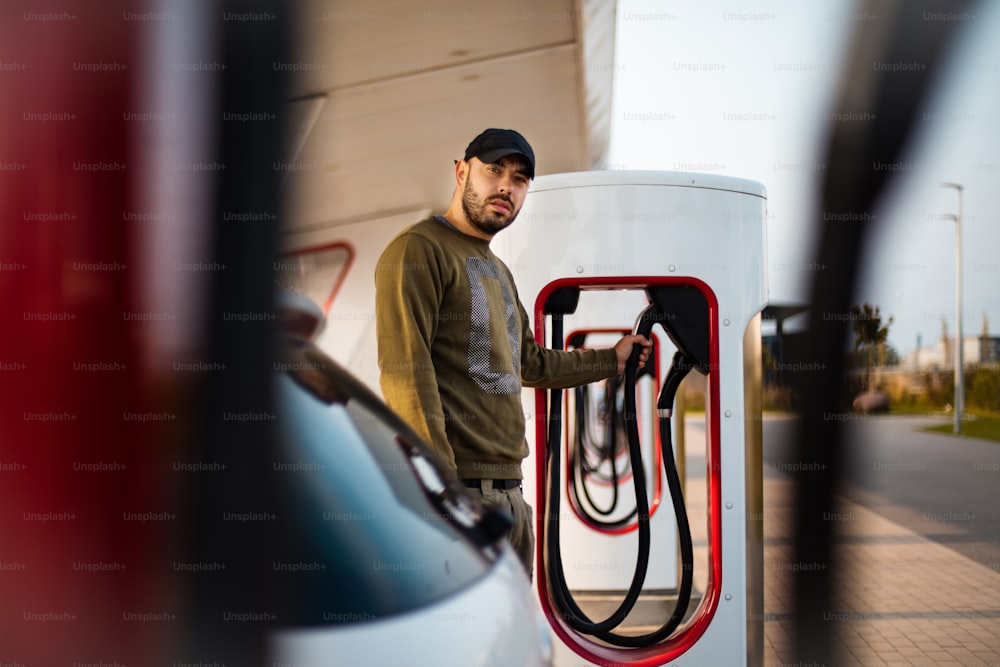 Un homme verse de l’essence dans sa voiture. L’accent est mis sur l’homme.  Pompe électrique pour voiture.