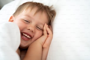 Cute little kid laughing to the camera, lying in bed. Sleepy head. Morning time.