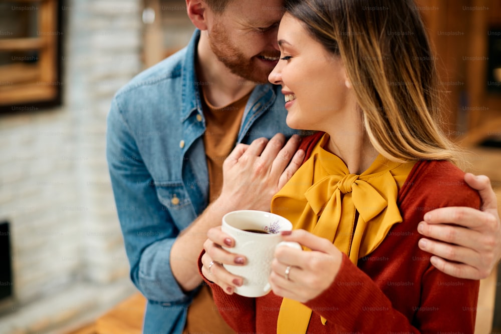 Young smiling couple enjoying in their love while having cup of coffee at home.