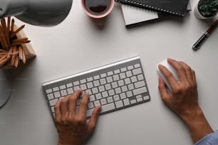 Above view of businessma hand typing on keyborad and holding mouse on white desk.