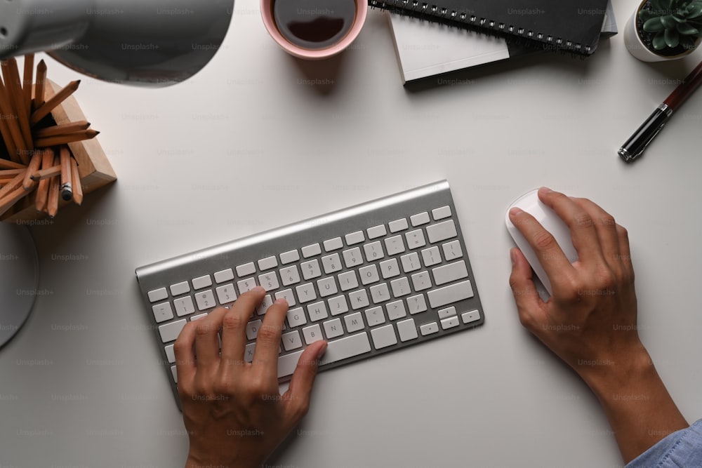 Vista superior de businessma escribiendo a mano en keyborad y sosteniendo el mouse en el escritorio blanco.