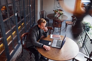 Top view of elegant young guy in formal wear that sits in cafe with his laptop.