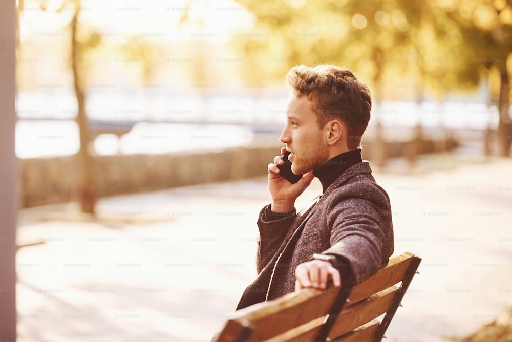 フォーマルな服を着た若い男は、晴れた日に秋の公園で電話をかけています。