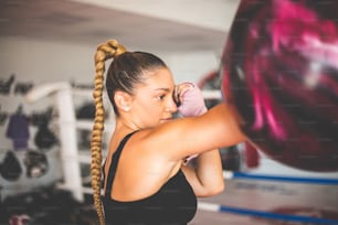 One woman, strong young lady with boxing gloves, punching a punching bag in gym alone. Focus is on woman.