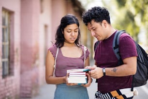 Two young students standing on street with books and talking.