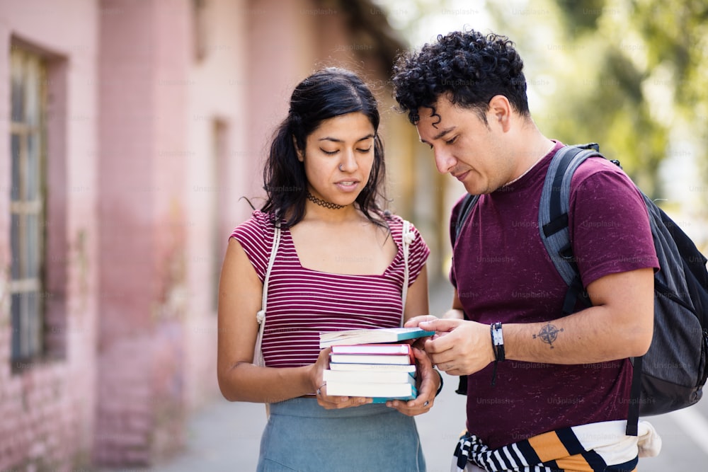 Two young students standing on street with books and talking.