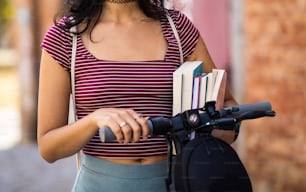 Young student girl with electric scooter and book on the street. Focus is on hand.