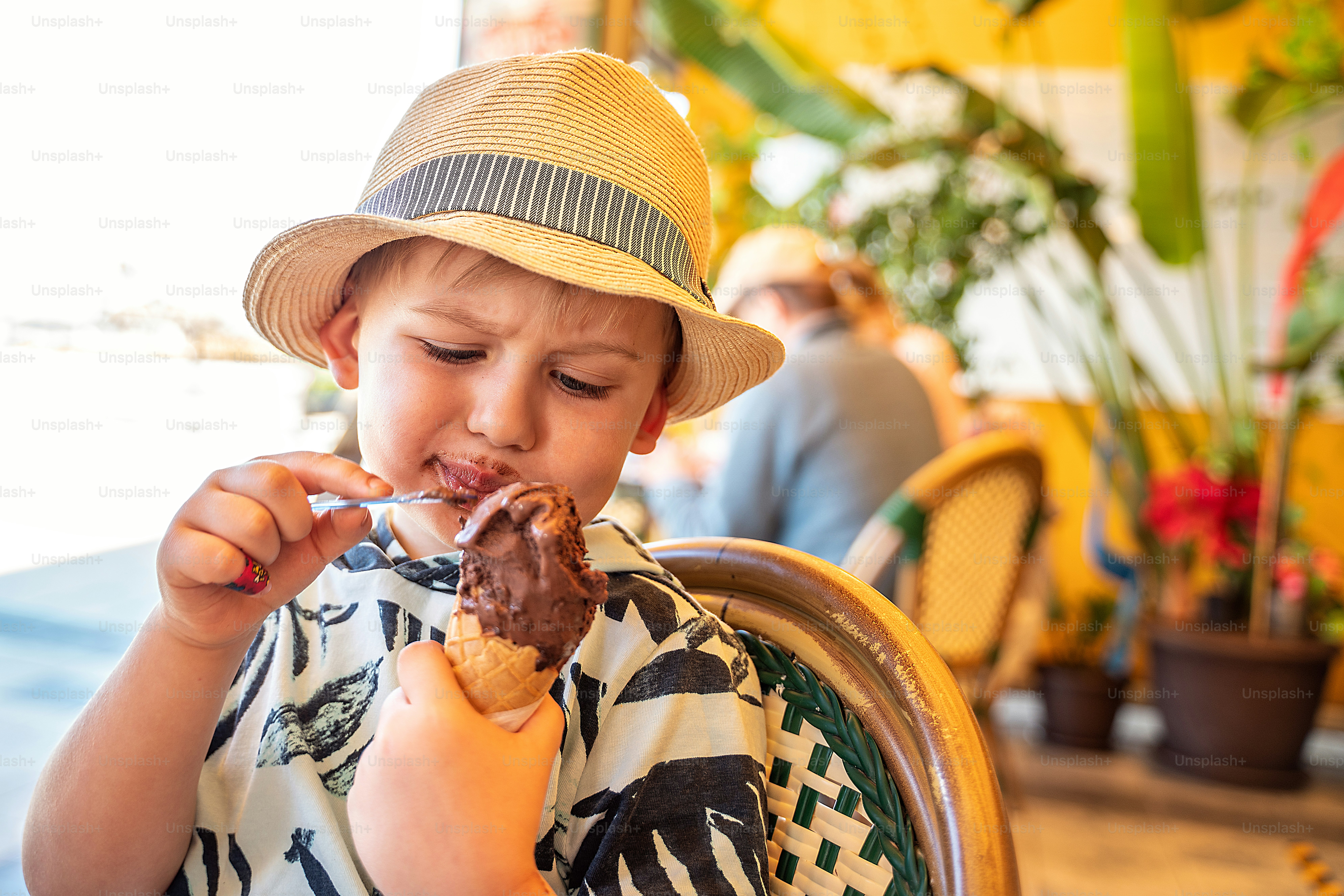 Little boy in summer hat eating chocolate ice-cream in waffle cone. Vacation happy time.
