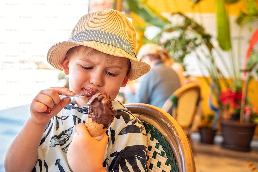 Little boy in summer hat eating chocolate ice-cream in waffle cone. Vacation happy time.