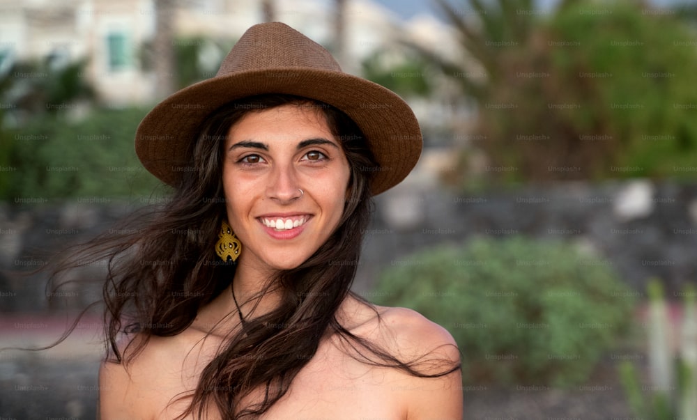 Mulher latina feliz com sorriso bonito vestindo chapéu elegante e olhando para a câmera. Mulher morena nova que desfruta de férias durante o verão. Menina alegre. Emoções de pessoas reais.
