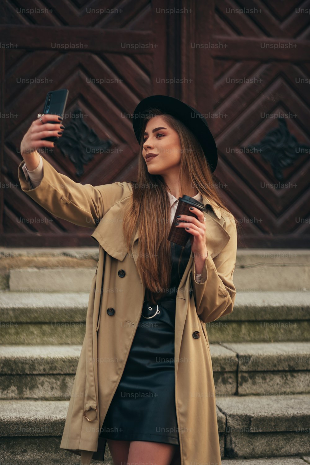 Young beautiful fashionable woman taking selfie with her smartphone while drinking coffee takeaway outside