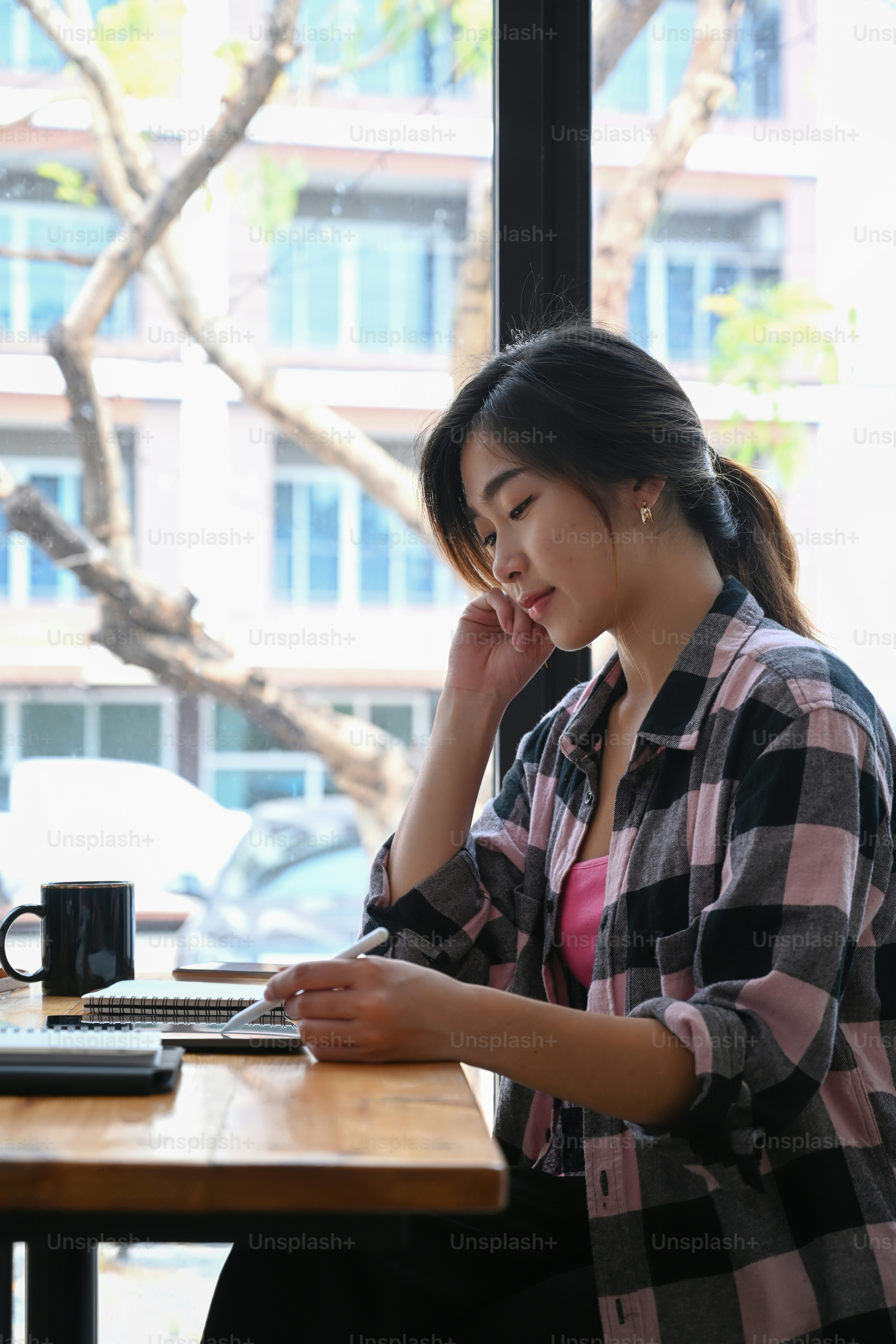 Side view of young woman creative designer sitting near window in coffee shop and working with computer tablet.