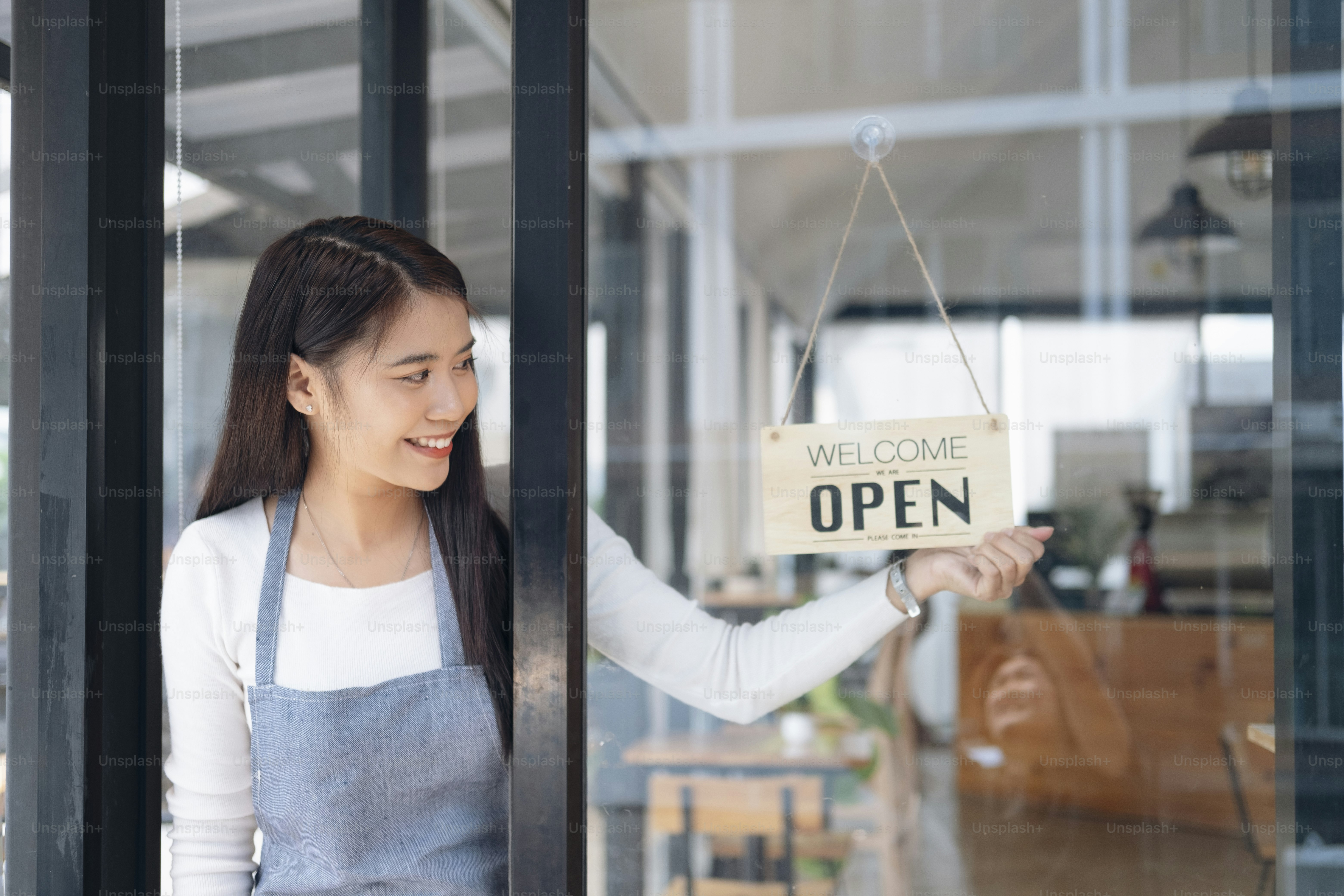 Small business owner smiling while turning the sign for the reopening of the place after the quarantine due to covid-19. Close up of womanÂÂ hands holding sign now we are open support local business.