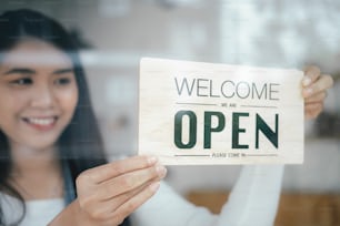 Small business owner smiling while turning the sign for the reopening of the place after the quarantine due to covid-19. Close up of womanÂÂ hands holding sign now we are open support local business.