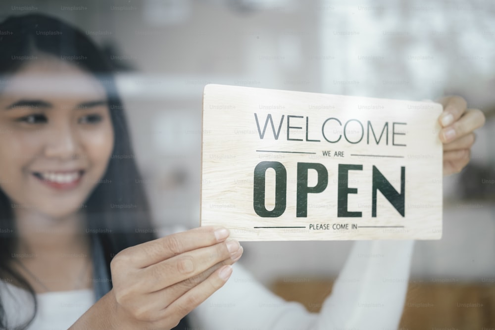 Small business owner smiling while turning the sign for the reopening of the place after the quarantine due to covid-19. Close up of womanÂÂ hands holding sign now we are open support local business.