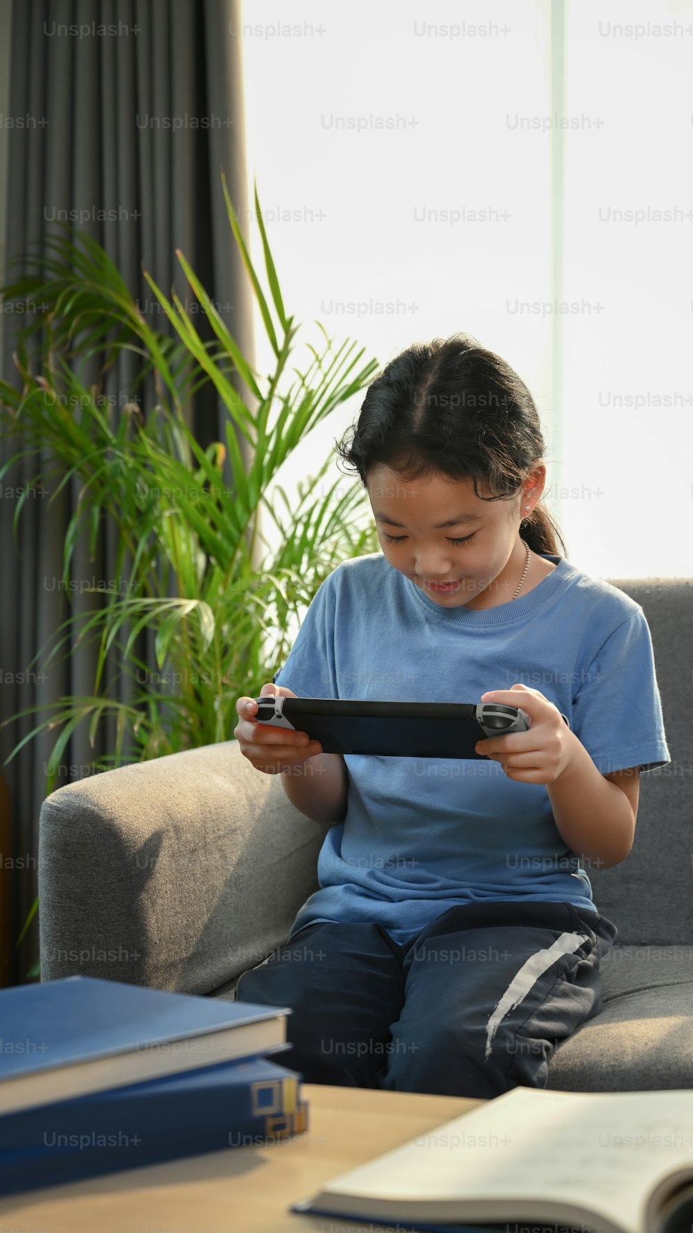Retrato da menina asiática jovem que joga jogos e sentada no sofá na sala de estar.