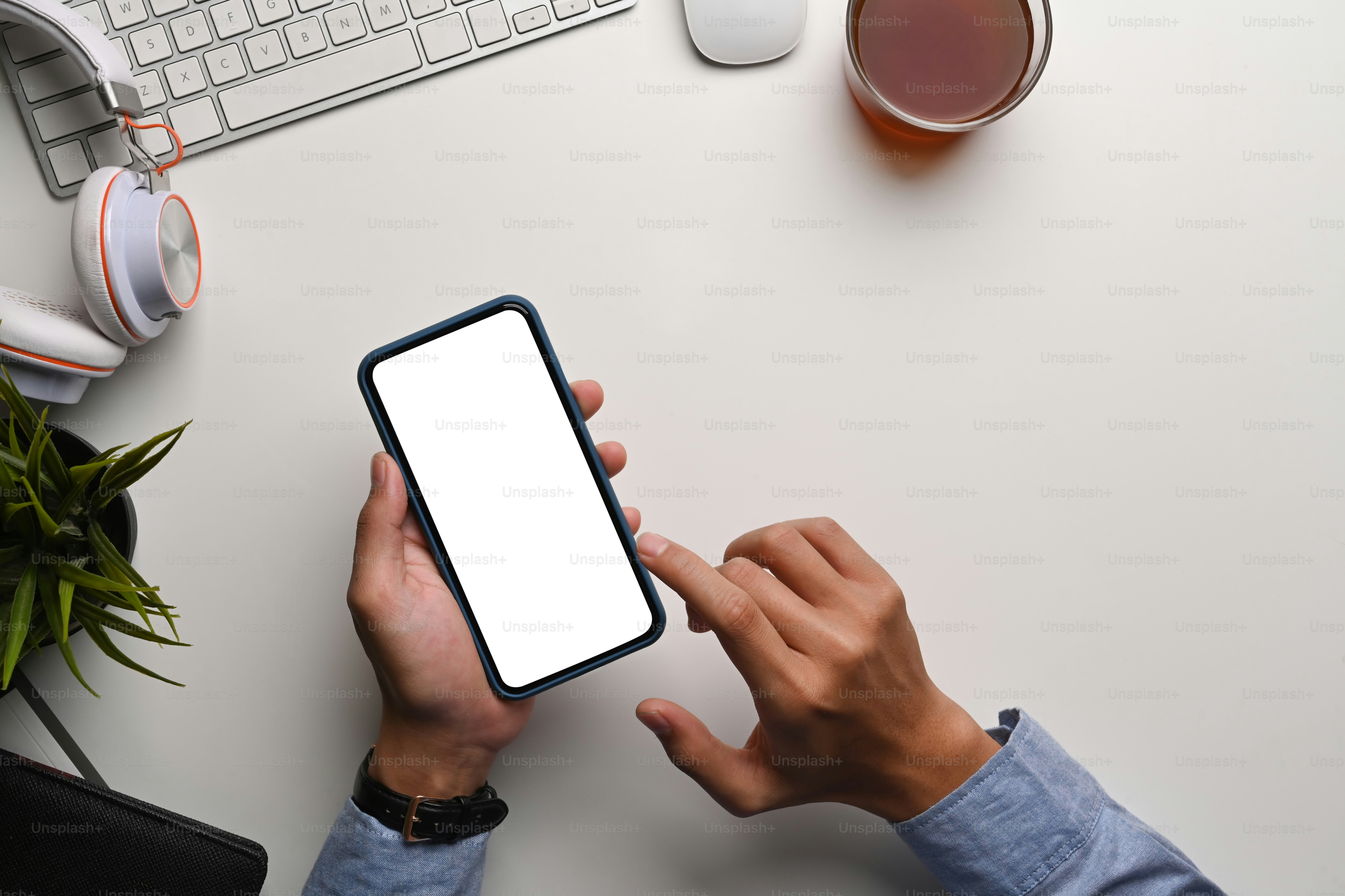 Above view of man holding and typing on smart phone at his workspace.