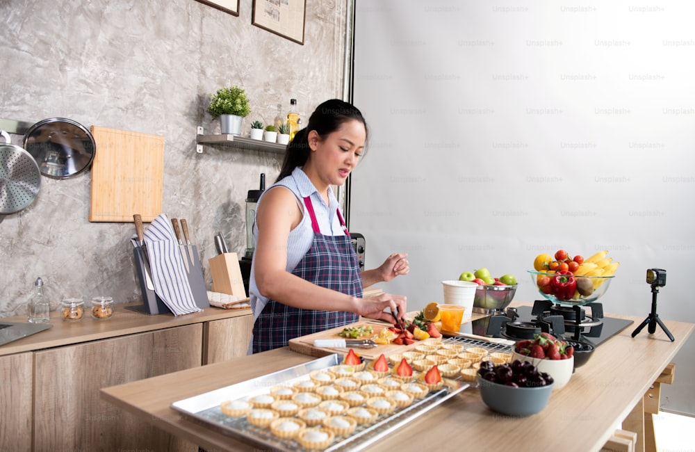 Asian woman making fruit tart for online selling delivery. Female small business owner entrepreneur use laptop and digital camera taking video of bakery to get order for customer. Work at home concept