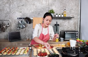 Asiatische Frau, die Obstkuchen für den Online-Verkauf herstellt. Weibliche Kleinunternehmerin Bäckerei Ladenbesitzerin, die in Laptop-Computer arbeitet, bekommt Auftrag für Kunde. Kleinunternehmen arbeiten zu Hause Konzept.