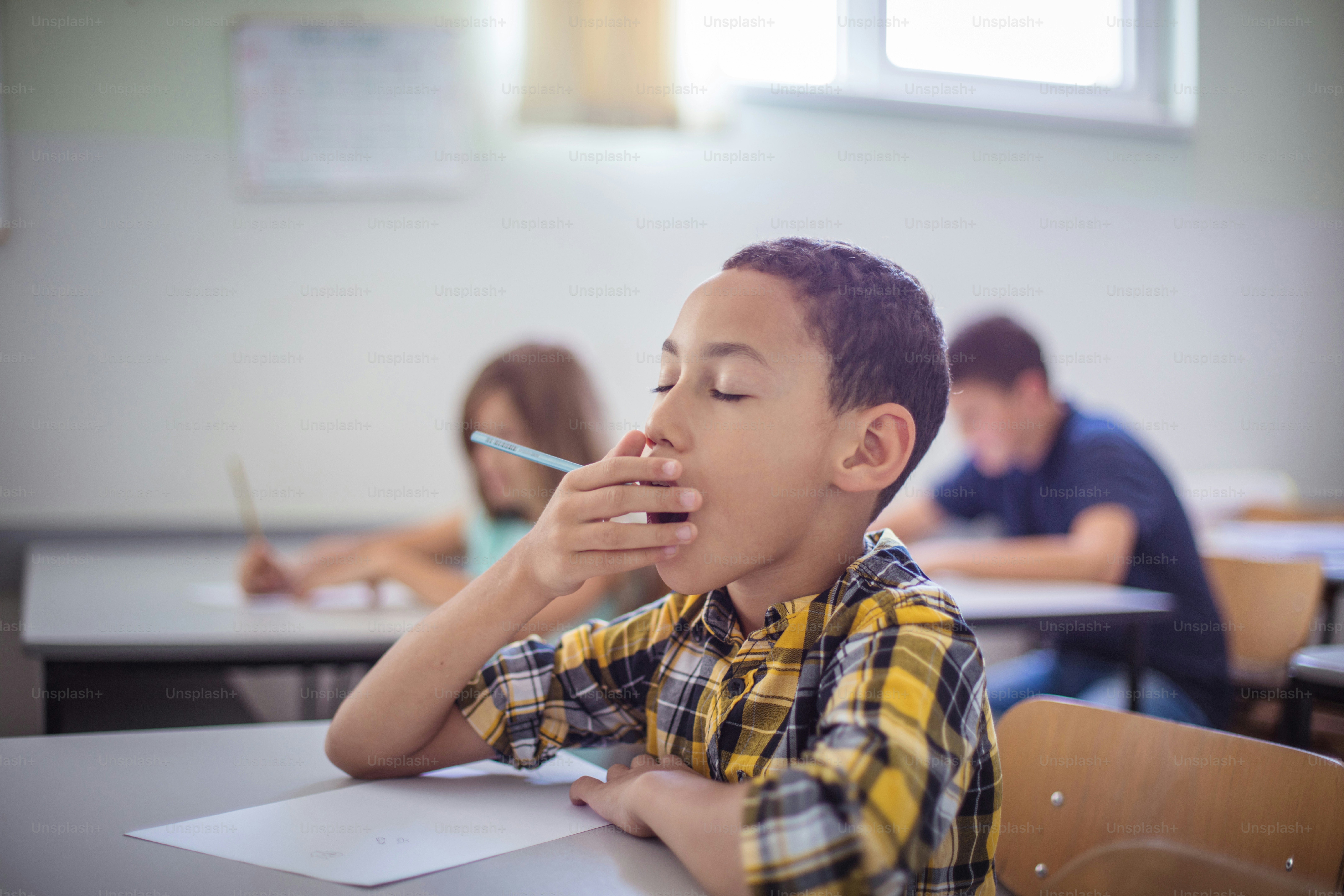 クラスであくびをする男子生徒。 教室に座っているティーンエイジャーの生徒。フォーカスは前景にあります